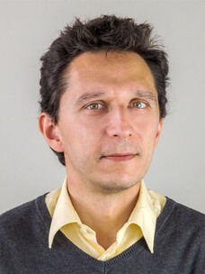 Vladimir Hinkov mit kurzem Haar, Hemd und Pullover vor grauem Hintergrund.